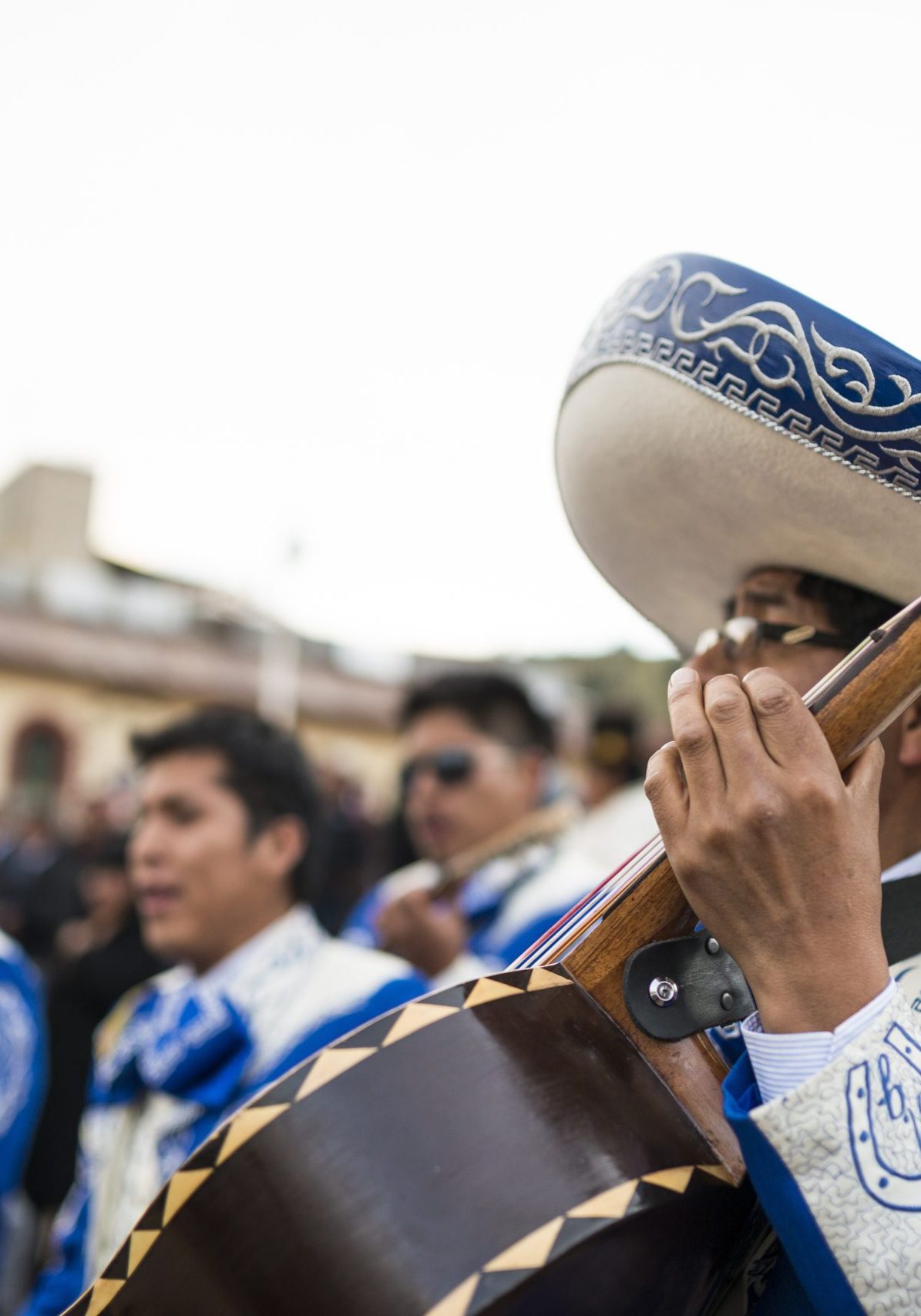 Mariachi musician strumming a guitar with a group of performers in the background. Mariachi musician strumming a guitar with a group of performers in the background.
